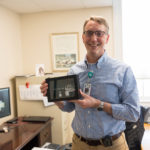 President and CEO Dan Bennett, holding a framed Gifford mask and empty vials from first doses of the COVID-19 vaccine